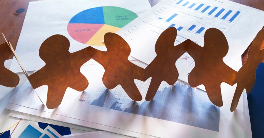 Cut out paper people holding hands standing up on a table full of financial documents to symbolise social value in the working world.