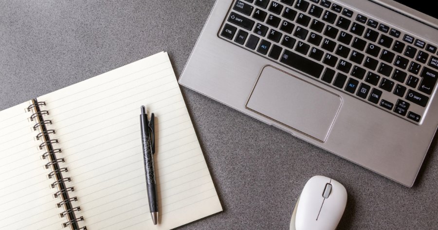 An image of a pad and laptop on a grey desk used to represent tender writing services